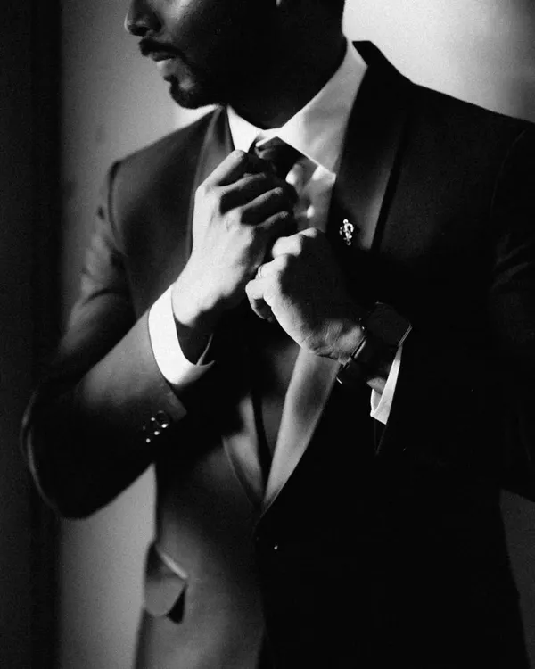 A moody and classic black and white shot of a groom adjusting his tie. This close-up focuses on the details and the sense of anticipation, creating a powerful and timeless image.