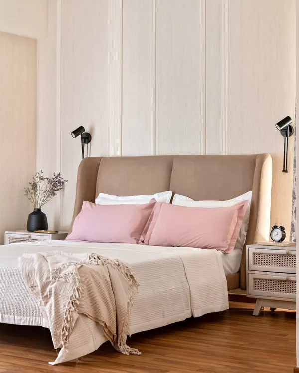 This serene bedroom features a winged headboard and fluted wall paneling in a light wood finish. The combination of soft textures, gentle colors, and adjustable wall sconces creates a perfect environment for relaxation.