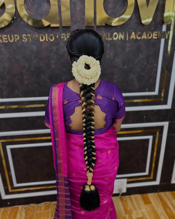 A classic South Indian bridal braid, neatly woven and adorned with a round arrangement of fresh jasmine flowers. This style is timeless and elegant.