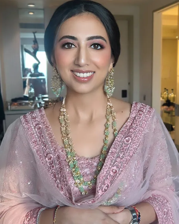 A happy and radiant wedding guest in a beautiful pink embroidered outfit. We created a fresh, glowing makeup look with pink tones and styled her hair in a sleek low bun to complement her elegant attire.