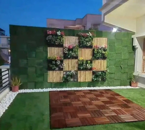 A beautiful green wall design combining an artificial grass base with bamboo panels and planter boxes for a textured, natural look. The wooden deck flooring provides a perfect yoga or seating spot.
