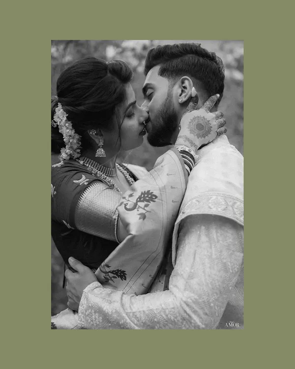 An intimate black and white portrait capturing a gentle kiss. The focus on the bride's traditional jewelry and the groom's tender embrace highlights the romantic essence of a Maharashtrian couple shoot.