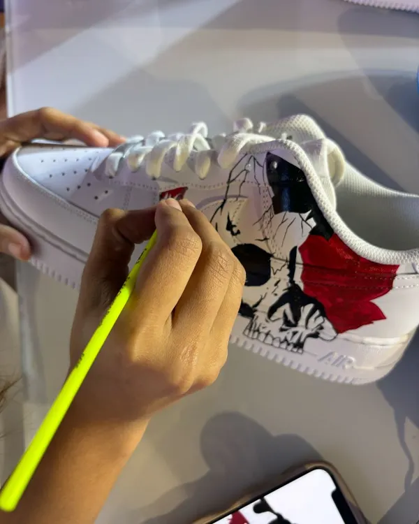 An artist adds color to a skull and rose design during a live painting session. Guests can watch up close as we transform a plain white sneaker into a piece of wearable art.
