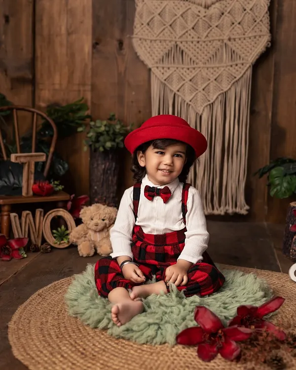 Two years old and full of style! This little gentleman, dressed in plaid overalls and a smart red hat, is celebrating his second birthday with a charming and rustic-themed portrait session.
