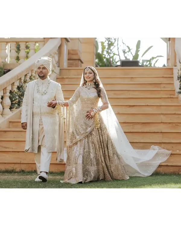 A picture of pure elegance. The couple makes their entrance in coordinated ivory and gold outfits. The bride's Tarun Tahiliani lehenga and the groom's Shantanu & Nikhil sherwani create a perfectly synchronized, regal statement for their wedding day.