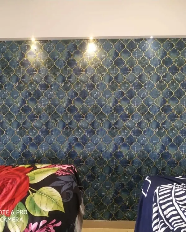 A stylish bedroom accent wall featuring a blue and grey geometric wallpaper with a subtle texture. The pattern adds a modern touch behind the bed.
