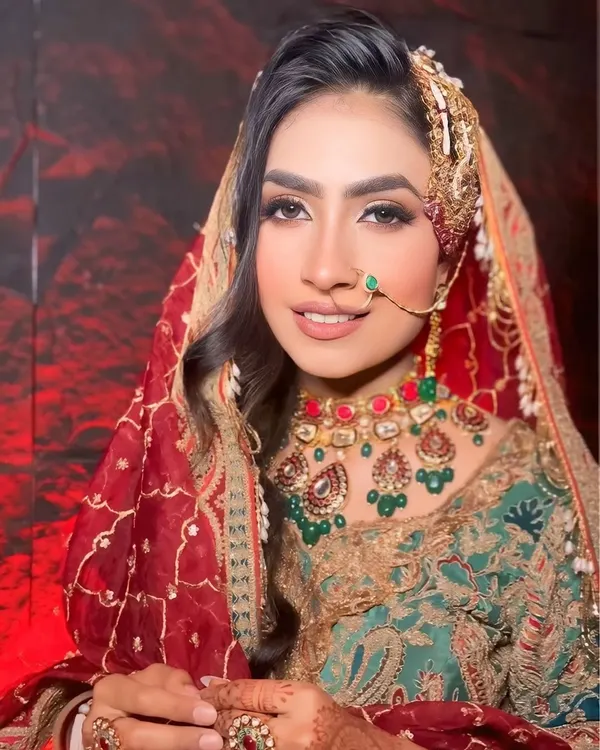 A close-up of a traditional Muslim bridal look. The focus is on soft, glowing makeup and a side-swept hairstyle adorned with a beautiful passa, creating a regal and elegant appearance.