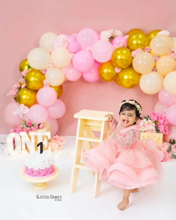 This is the kind of pure, uncontainable joy I aim to capture in my first birthday photoshoots. This little one's laughter, surrounded by a beautiful pink and gold balloon setup with a glowing "ONE" sign, is a perfect memory of such a special milestone.