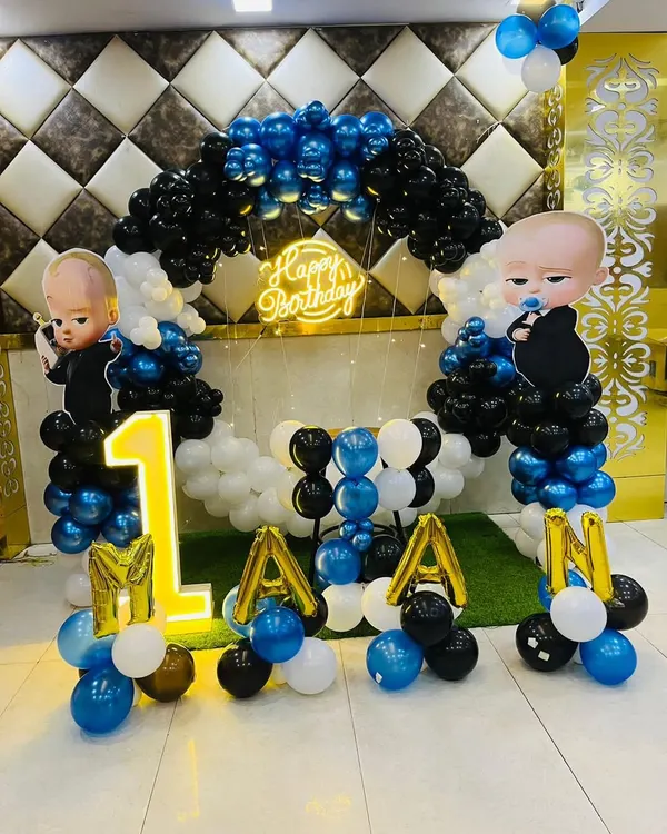A classic Boss Baby theme for a first birthday. This setup includes a balloon arch in blue, black, and white, character cutouts, a 'Happy Birthday' neon sign, and a light-up number '1'.