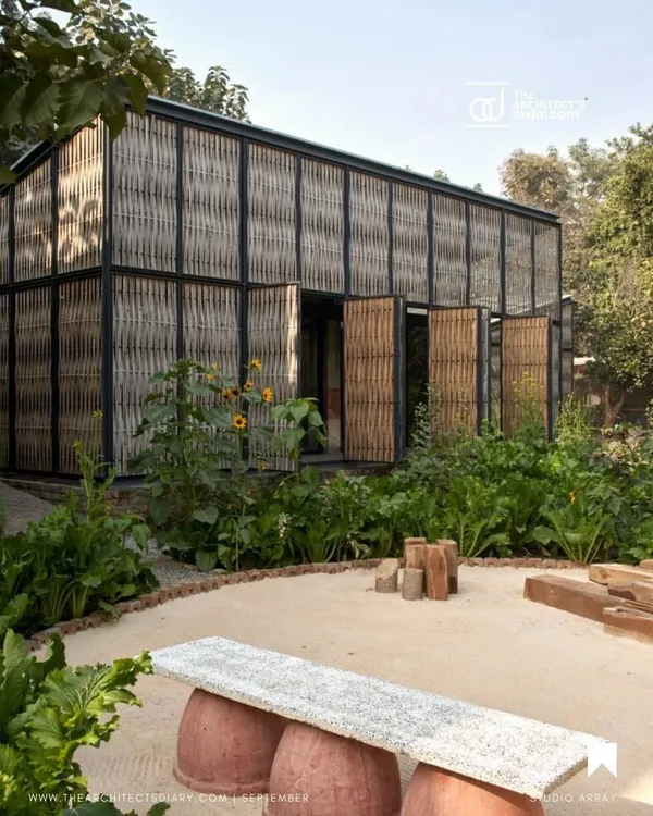 The Artist Residency at Farm8, nestled in a lush green landscape. The structure's facade is a screen of woven bamboo set within a steel frame, creating a porous skin that breathes and allows the building to merge with its organic surroundings.
