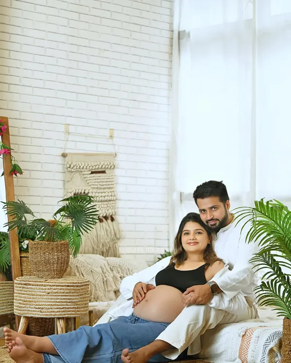 A relaxed and casual maternity portrait of a couple in a bright, bohemian-style studio setting. This image captures their comfortable intimacy and excitement.