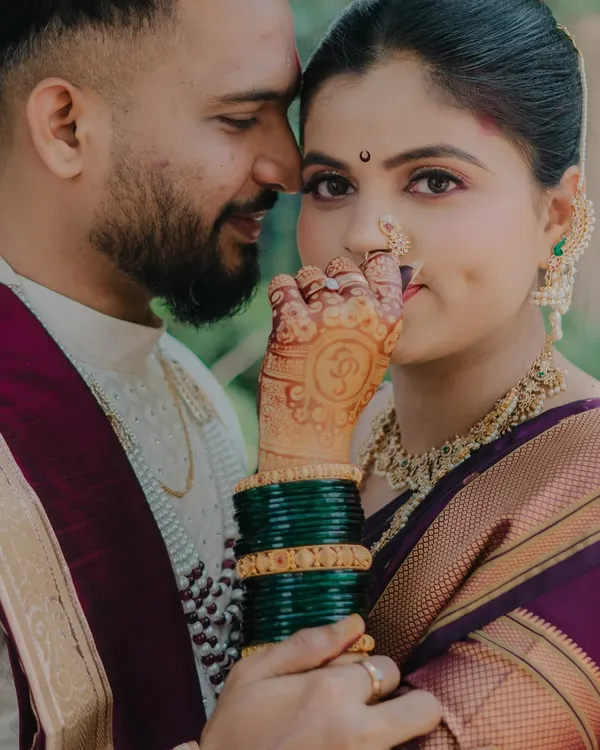 A close-up portrait focusing on the bride's intricate henna and traditional Maharashtrian jewelry. The way she holds her hand near her face draws attention to the beautiful nath and her expressive eyes, creating an intimate and culturally rich image.
