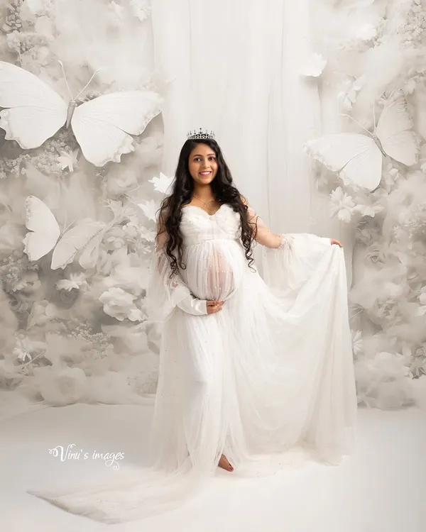 A heavenly scene surrounded by clouds and white butterflies. This portrait captures the magical transformation of motherhood, with the mother-to-be looking like a queen in her own butterfly garden.