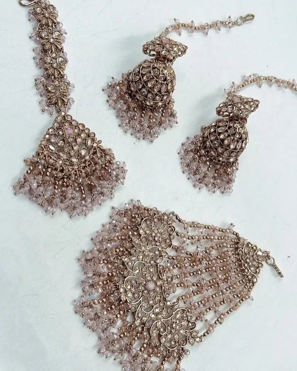 A beautiful mehndi jewelry set in a dusty pink shade. The set includes a maang tikka, jhumkas, and a hathphool, all adorned with delicate beads.