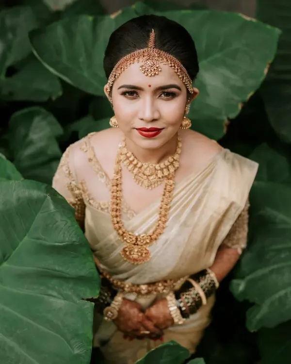 A striking bridal portrait where the bride, in her traditional gold and cream saree, is framed by lush green leaves. We use natural elements to create artistic and memorable portraits that highlight the bride's elegance and personality.