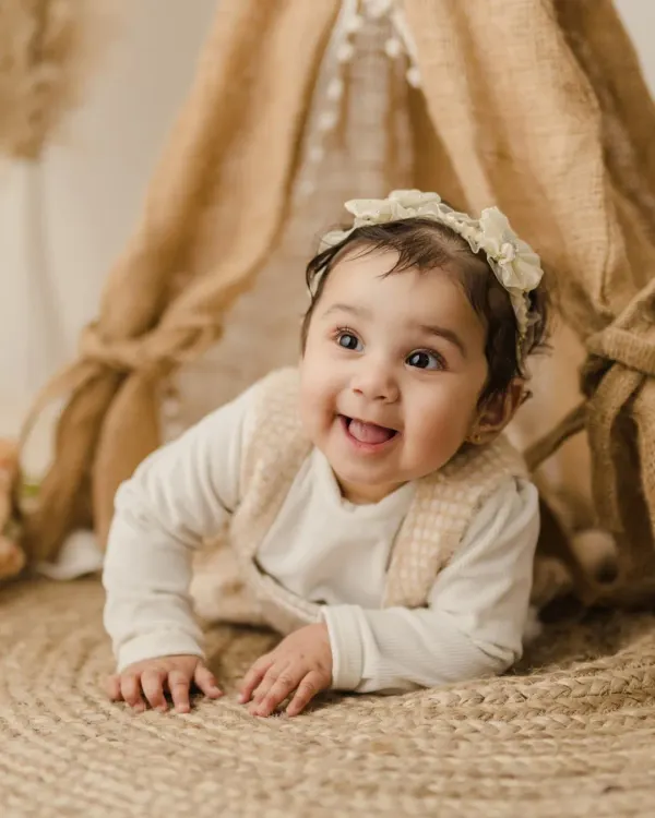 A beautiful shot of a baby girl during her sitter session, crawling on a soft jute rug with an inquisitive and happy expression.