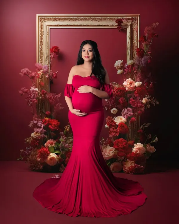 A stunning studio portrait featuring a gorgeous mom-to-be in a classic red off-shoulder gown. The floral frame adds a touch of romance and artistry to this elegant maternity photo.