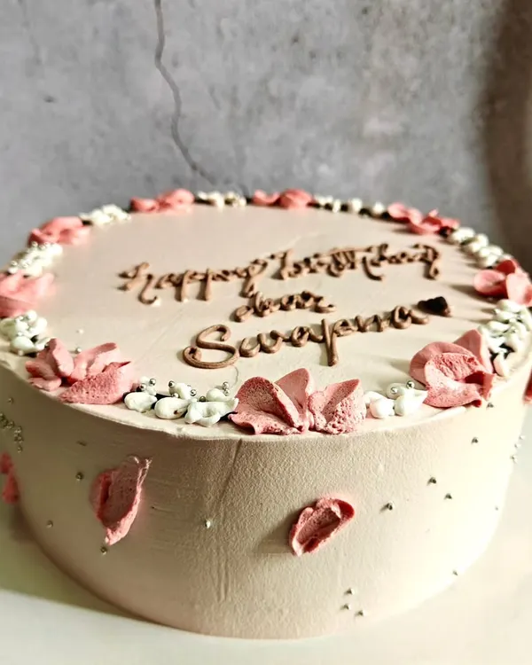 A simple and elegant cake with delicate pink floral details and a personalized message, proving that sometimes less is more.