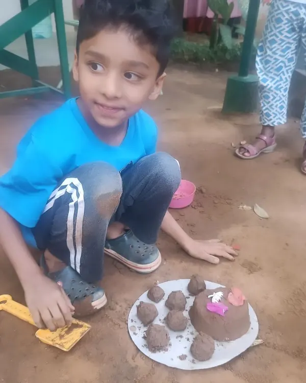 A young boy proudly displays his mud cake creation. This sensory activity allows children to explore textures and shapes using natural materials.