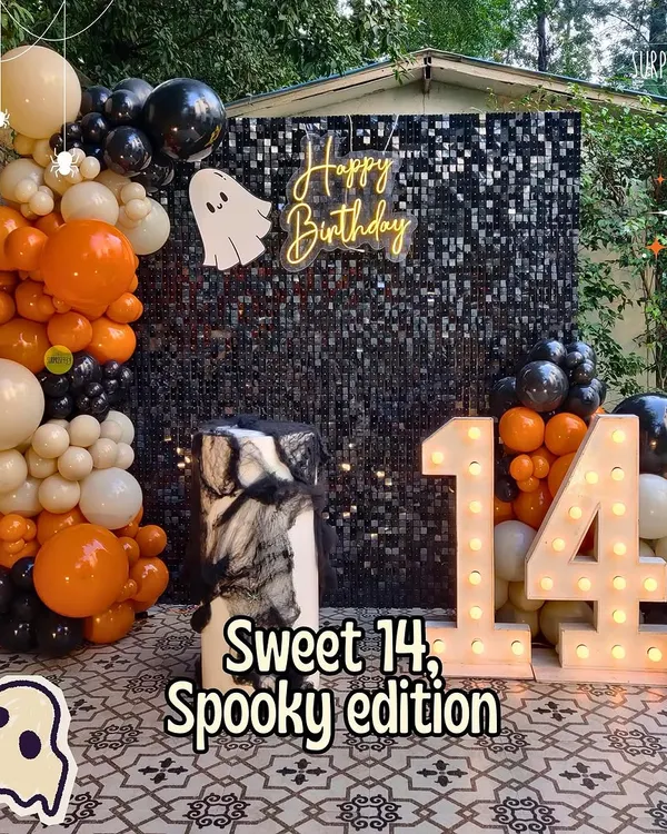 Sweet 14, spooky edition! For this Halloween-themed birthday, we designed a black sequin backdrop with a ghostly neon sign, marquee numbers, and a balloon garland in classic orange, black, and white.
