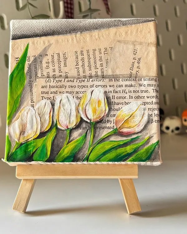 A beautiful mini canvas painting of white tulips against a vintage-inspired background of old book pages. This piece, created with jelly acrylics, comes with a mini easel for easy display.
