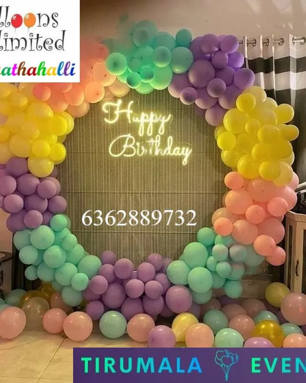 A beautiful pastel rainbow balloon ring with a 'Happy Birthday' neon sign, creating a perfect photo corner in a home.