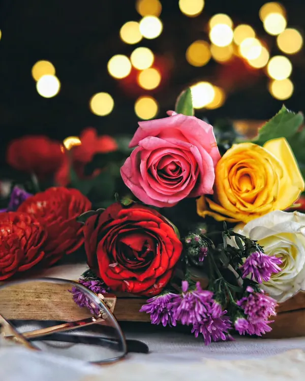 A moody and romantic still life of colorful roses on an open book, with soft bokeh lights creating a magical and dreamy atmosphere.