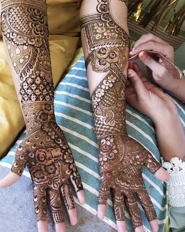 A moment from a mehendi session, showing the application process. You can see the name 'Salman' being intricately woven into the palm, and the half-finished design on the other arm.