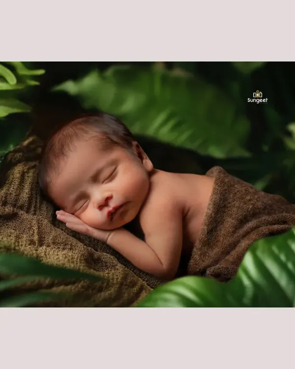 Tucked away in a lush, green world of his own. This nature-inspired newborn shot uses soft textures and deep greens to create a peaceful, organic feel, highlighting the baby's serene expression.