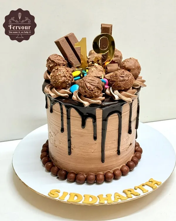 A chocolate overloaded cake for a 19th birthday. This tall drip cake is covered in chocolate frosting and topped with Ferrero Rocher, KitKats, and Gems.