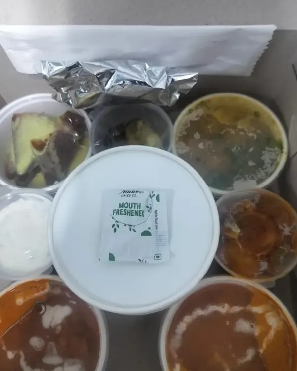 An overhead view of our executive meal box. This thali-style packaging includes multiple curries, raita, dessert, and a mouth freshener, ensuring a complete and satisfying lunch.