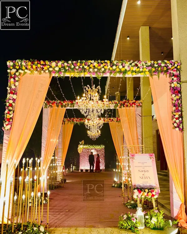 A beautiful entrance sets the tone for the entire evening. Here, I combined elegant peach-colored drapes, intricate floral arrangements, warm candle-like lighting, and grand chandeliers to create a welcoming and luxurious entryway for the guests.