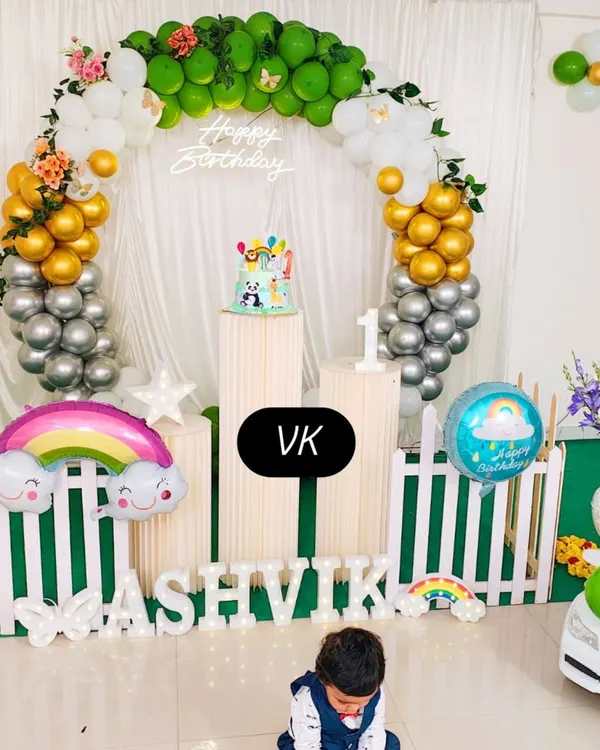 A full view of my decoration work for a first birthday. This setup includes a circular balloon arch in green, gold, and silver, custom name lettering, and themed props like the rainbow foil balloon to create a complete look.