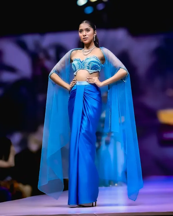 A stunning shot from Bangalore Fashion Week. The model's powerful pose and the flowing blue cape create a dramatic and memorable runway moment.
