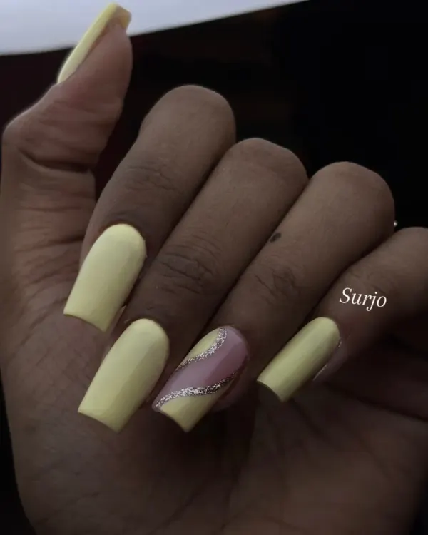 A simple yet sunny look. This manicure features long, square shaped nails in a matte pastel yellow, with a single accent nail featuring a diagonal silver glitter stripe.