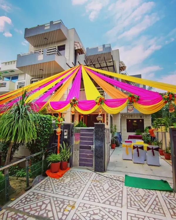 For home-based functions like a Mehandi or Sangeet, I transform the entire front of the house. Here you can see a full canopy of bright pink and yellow fabric drapes, creating a festive atmosphere right from the street.