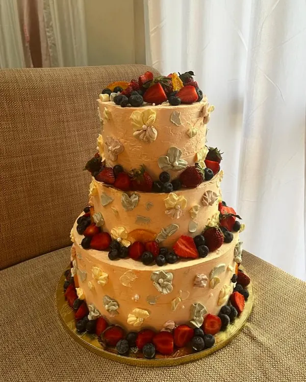 This 10kg, three-tiered vanilla sponge cake was infused with orange zest and decorated with Swiss meringue buttercream, fresh berries, and palette knife flowers for a grand celebration.