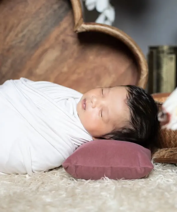 A classic newborn portrait, with the baby swaddled in white and sleeping peacefully on a soft rug. Simple, pure, and timeless.