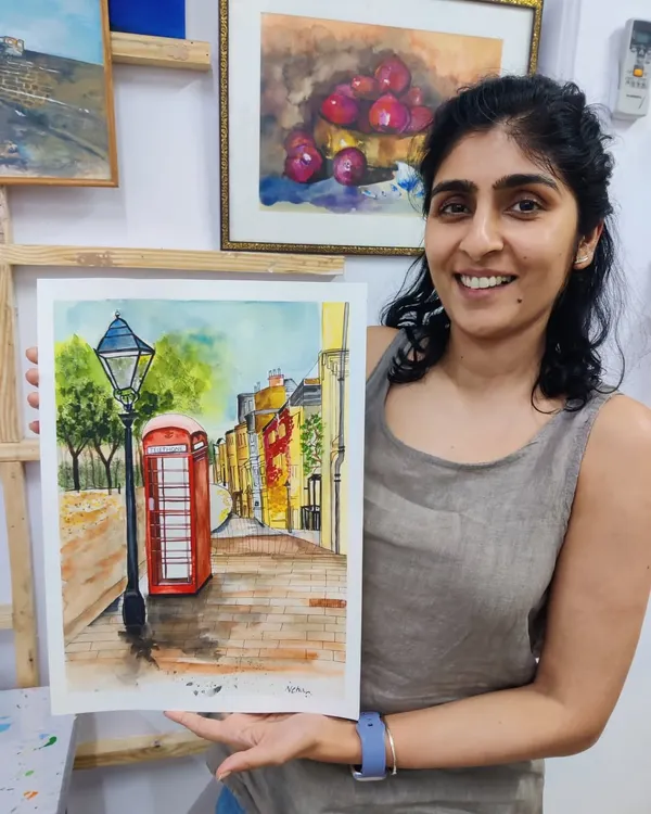 A student proudly displays her completed watercolor painting of a classic London street scene, featuring a red telephone booth. This piece shows excellent control of the medium and attention to architectural detail.