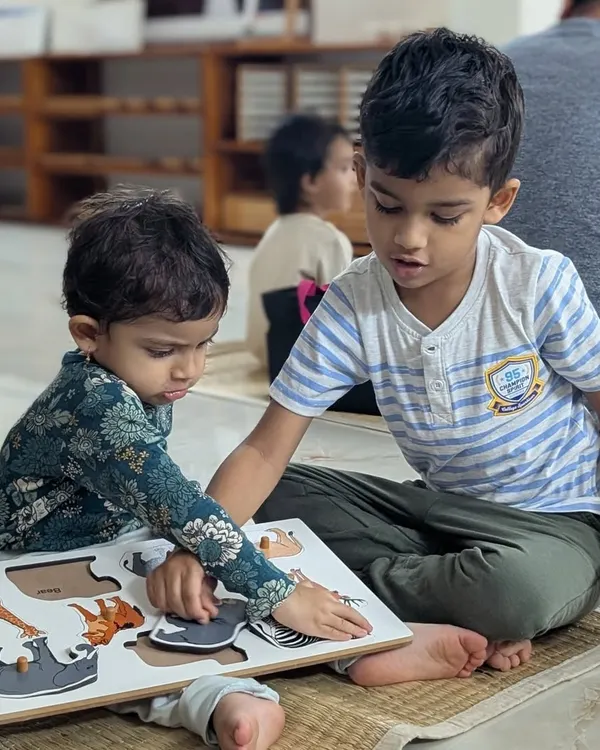 This is what our mixed-age environment is all about. Here, an older child, one of our alumni, gently guides his younger sister on her first day, helping her with an animal puzzle. It’s a beautiful moment of natural leadership and care.