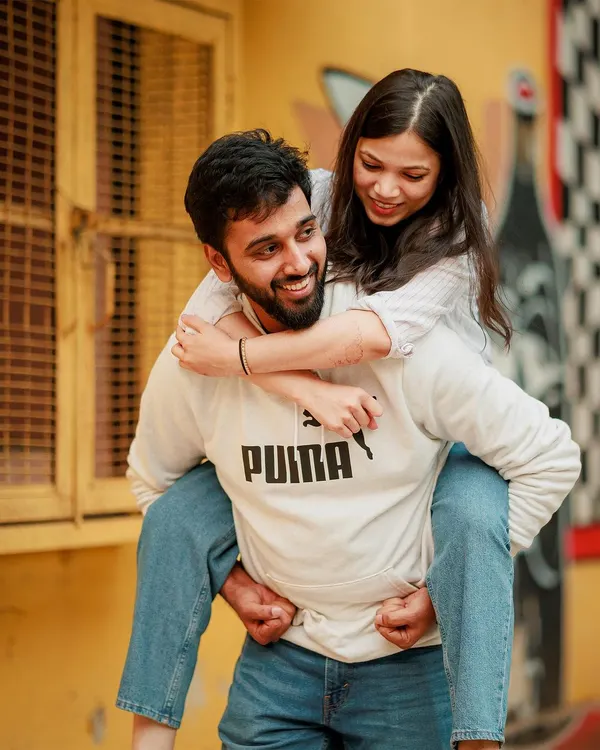 A fun and spontaneous piggyback moment from a casual pre-wedding shoot in Delhi. This image perfectly captures the playful and carefree dynamic of the couple against a vibrant, artistic city wall.