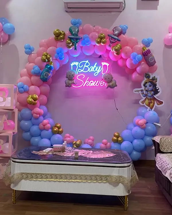 A beautiful Kanha ji themed baby shower, perfect for a divine blessing. This setup features a circular balloon arch in pink and blue, a glowing neon "Baby Shower" sign, and cutouts of Radha and Krishna.