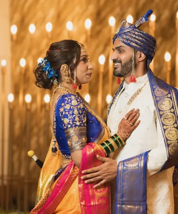 A royal portrait of a Maharashtrian couple in stunning traditional attire, with the groom in a royal blue turban and the bride in a vibrant Paithani saree.