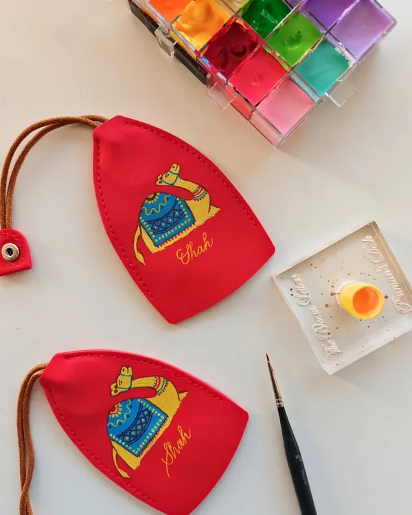 The details are what I love most. Here, I'm hand painting a colorful camel illustration and adding the family name 'Shah' to a bright red leather keychain, creating a vibrant and personal accessory.