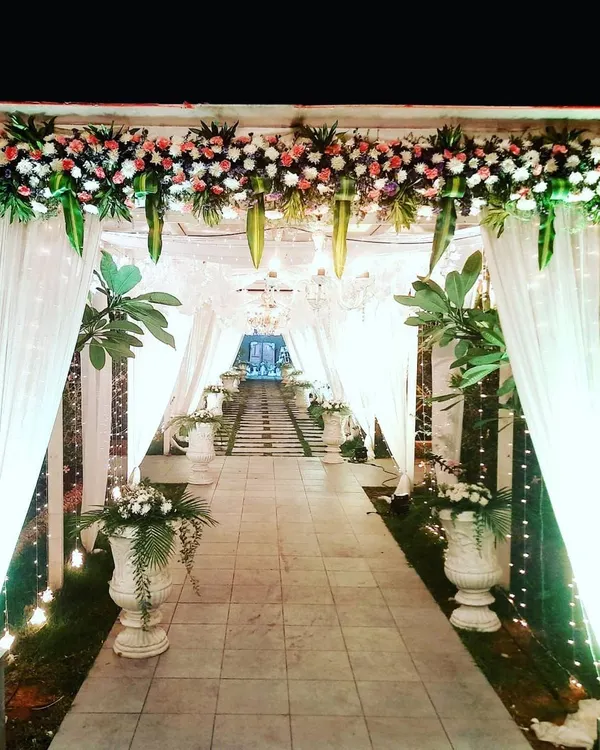 I created this magical entrance tunnel for an outdoor wedding using flowing white drapes and fairy lights. The path is lined with floral arrangements in classic white urns, guiding guests toward the main event area.