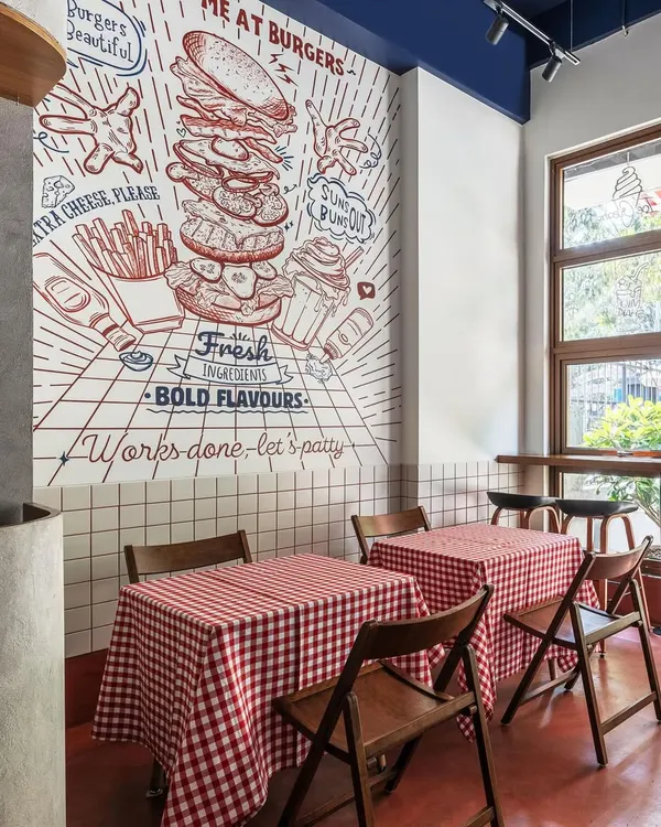 The hero of this diner's interior is the hand-drawn style mural, which we designed to capture the fun and flavor of the brand. It serves as a dynamic backdrop to the dining area, which features classic red-and-white checkered tablecloths.