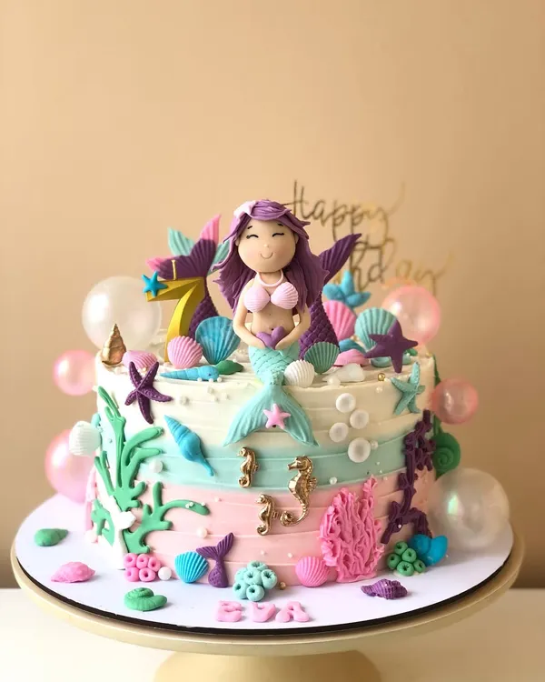 An underwater dream, this mermaid cake is decorated with pastel buttercream waves, edible shells, starfish, and a beautiful mermaid topper.