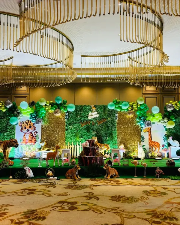A wide shot of a grand jungle theme stage in a large hall, showing the scale of the setup with multiple animal props and green foliage backdrops.