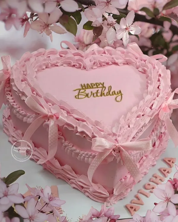 A stunning pink vintage heart cake. This design features intricate, frilly piping and delicate ribbon bows, perfectly capturing the romantic coquette aesthetic.