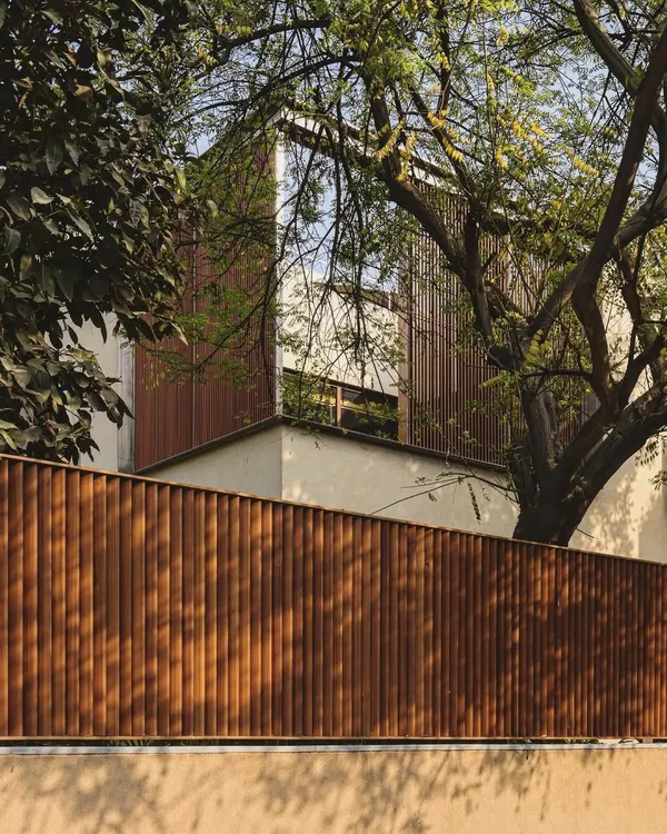 A facade composed of vertical wooden louvers provides privacy and shade while allowing for natural ventilation. This skin gives the building a warm, textured appearance that is rooted in its natural surroundings.